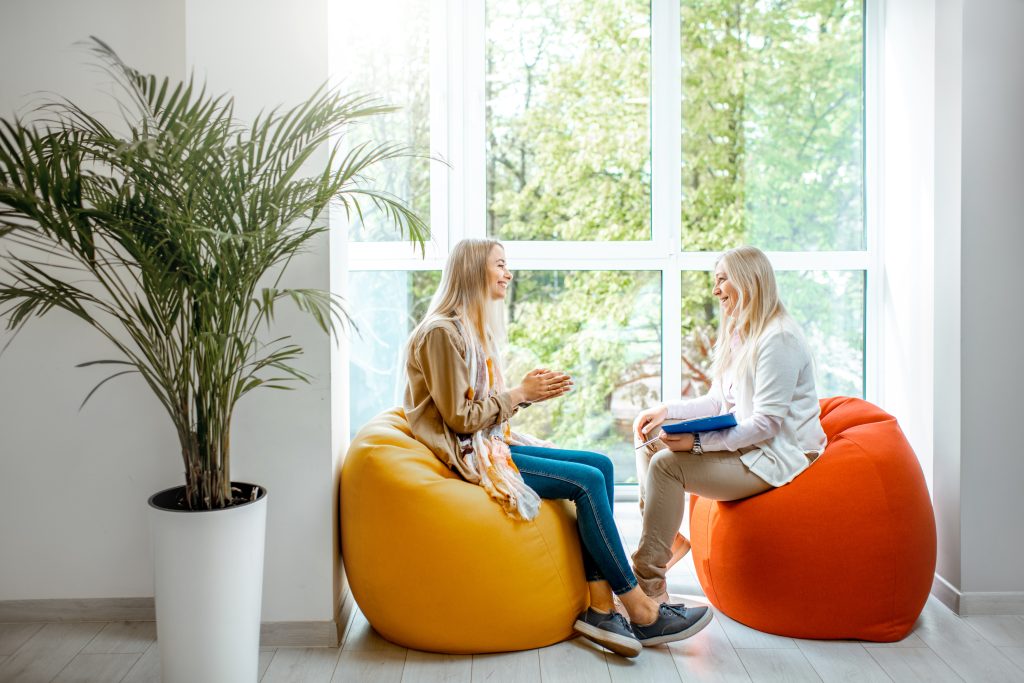 Two females conversing on bean bags near a window