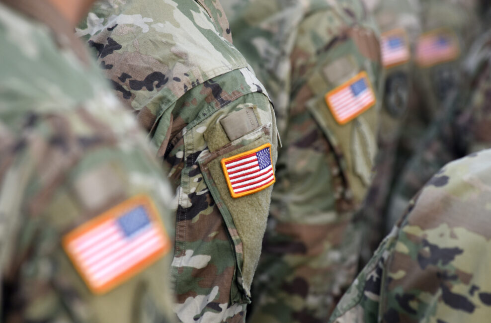 A soldier in a camouflage suit proudly displays the US flag on their shoulder